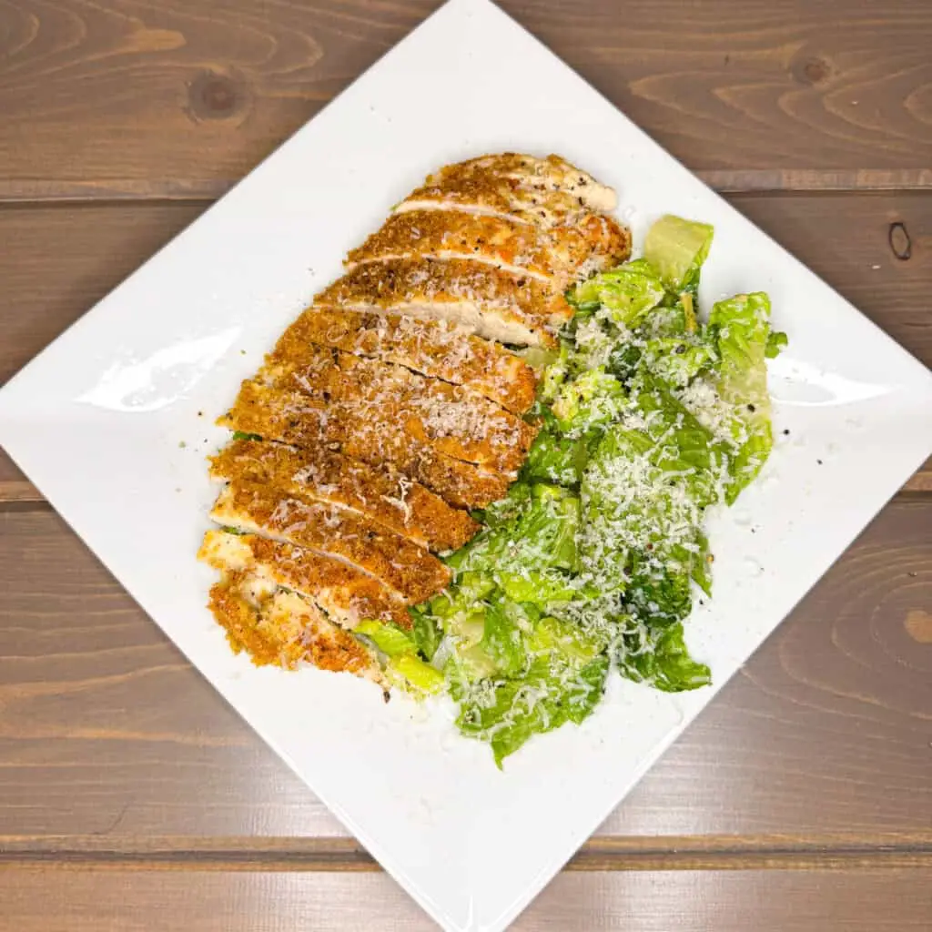 This high-protein dish features crispy chicken coated in crushed pork rinds, served on a bed of romaine lettuce with a homemade creamy Caesar dressing.