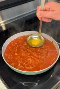 Dropping a fresh cracked egg into a rich beef, tomato sauce