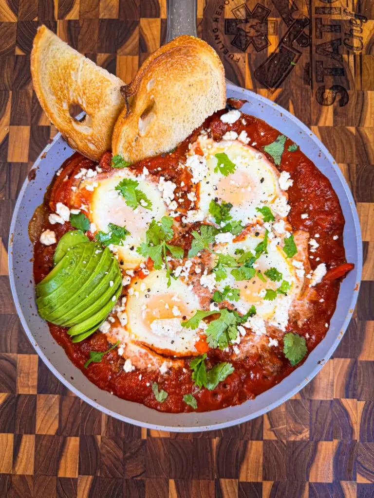 hearty, protein-packed dish combining spiced ground beef, baked eggs, and a flavorful tomato sauce, topped with creamy avocado, tangy feta, and fresh cilantro.